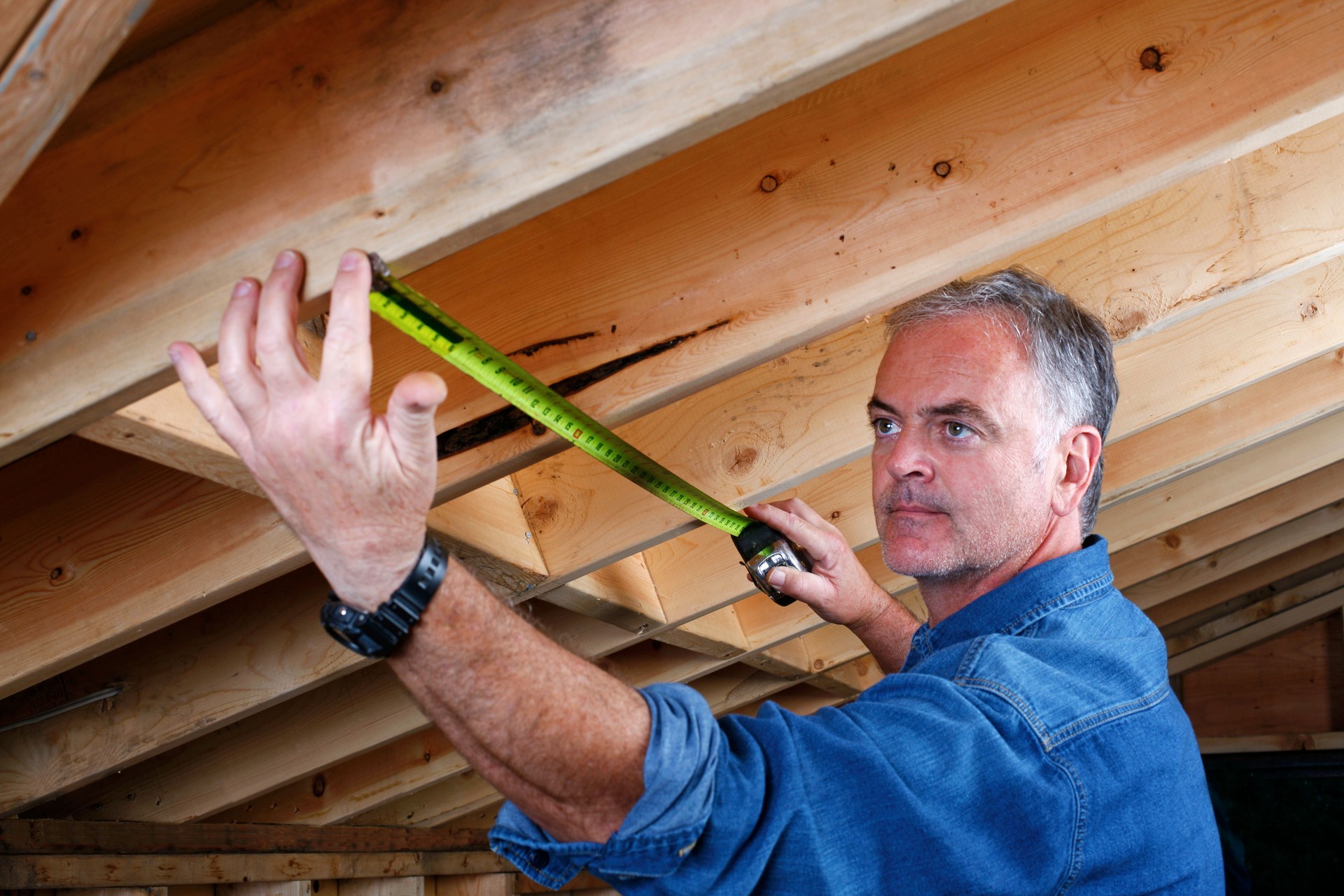 Man measuring distance between rafter beams of home addition.